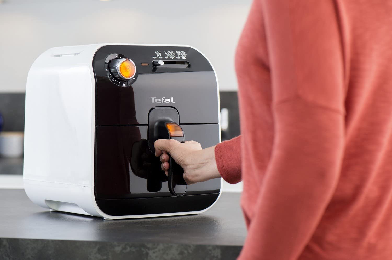 Main tirant le tiroir du Tefal Fry Delight FX100015, cadran minuterie orange allumé et repères de cuisson visibles sur le bandeau noir
