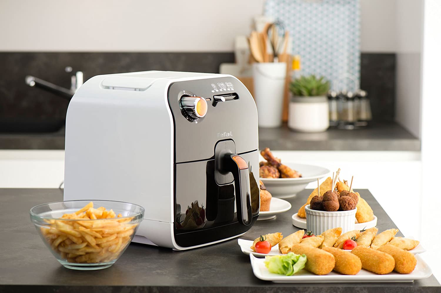 Tefal Fry Delight FX100015 blanc posé sur un plan de travail, entouré de frites, nuggets et boulettes dorés servis à l'assiette