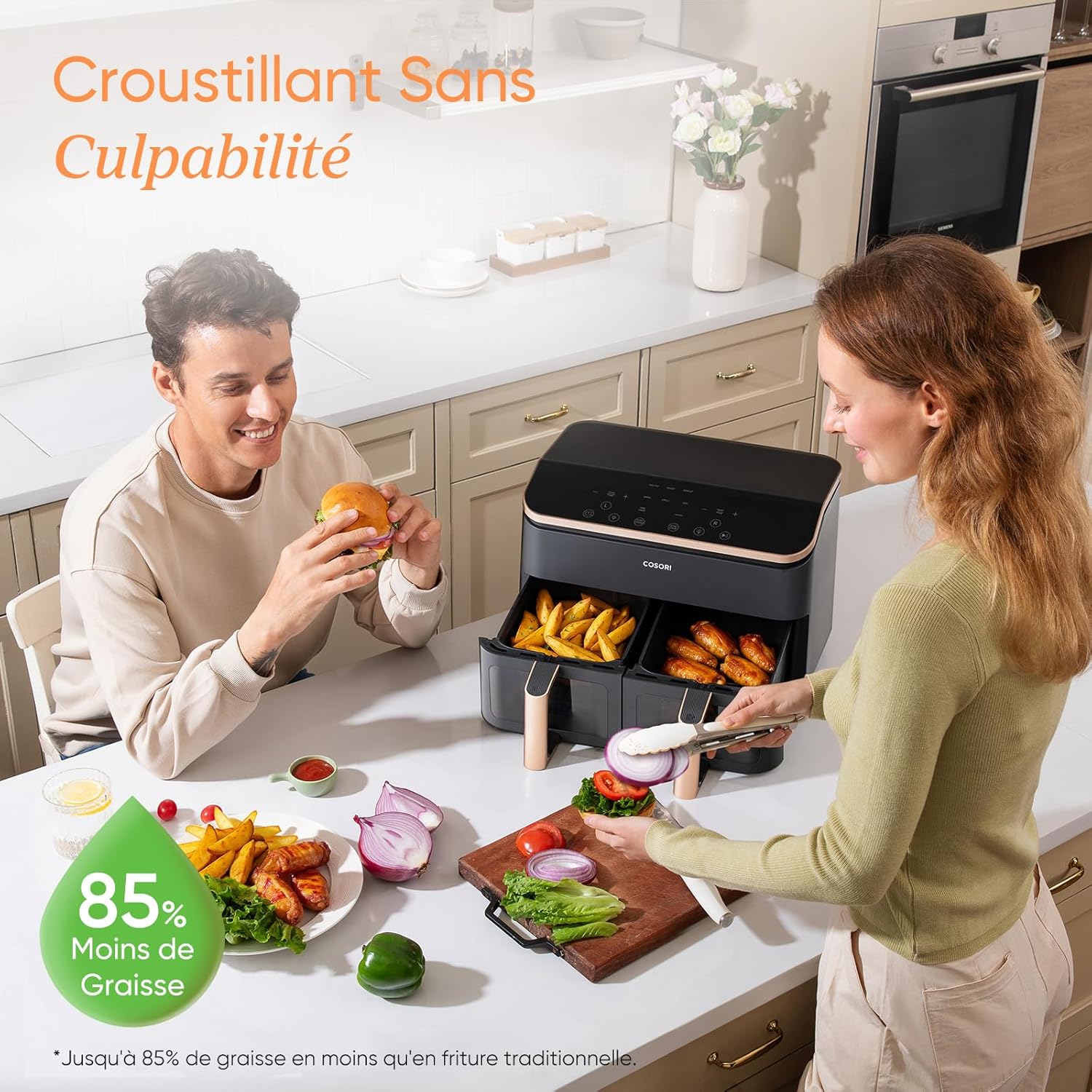 Cosori R903 posé sur un îlot de cuisine, ses deux tiroirs ouverts sur des frites et des ailes de poulet, un couple préparant le repas autour