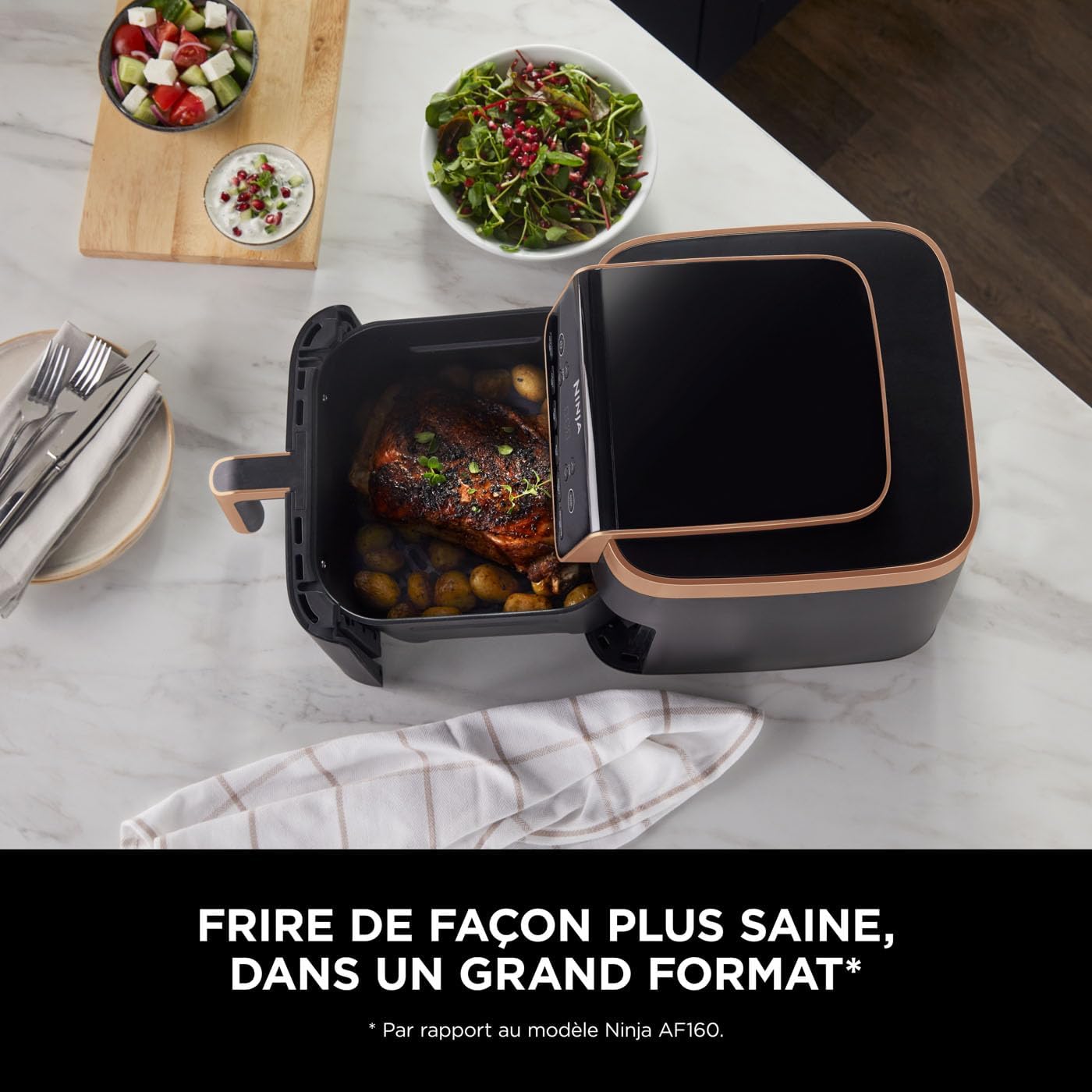 Tiroir carré du Ninja MAX PRO sorti sur un plan de travail en marbre, garni d'un rôti et de pommes de terre grenailles, à côté de salades servies en bols