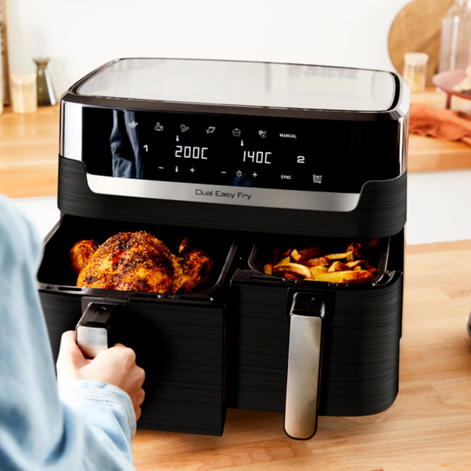 Airfryer Tefal Dual Easy Fry EY901810 posé sur un plan de travail en bois, ses deux tiroirs tirés sur un poulet entier doré dans la grande cuve et des frites dans la petite
