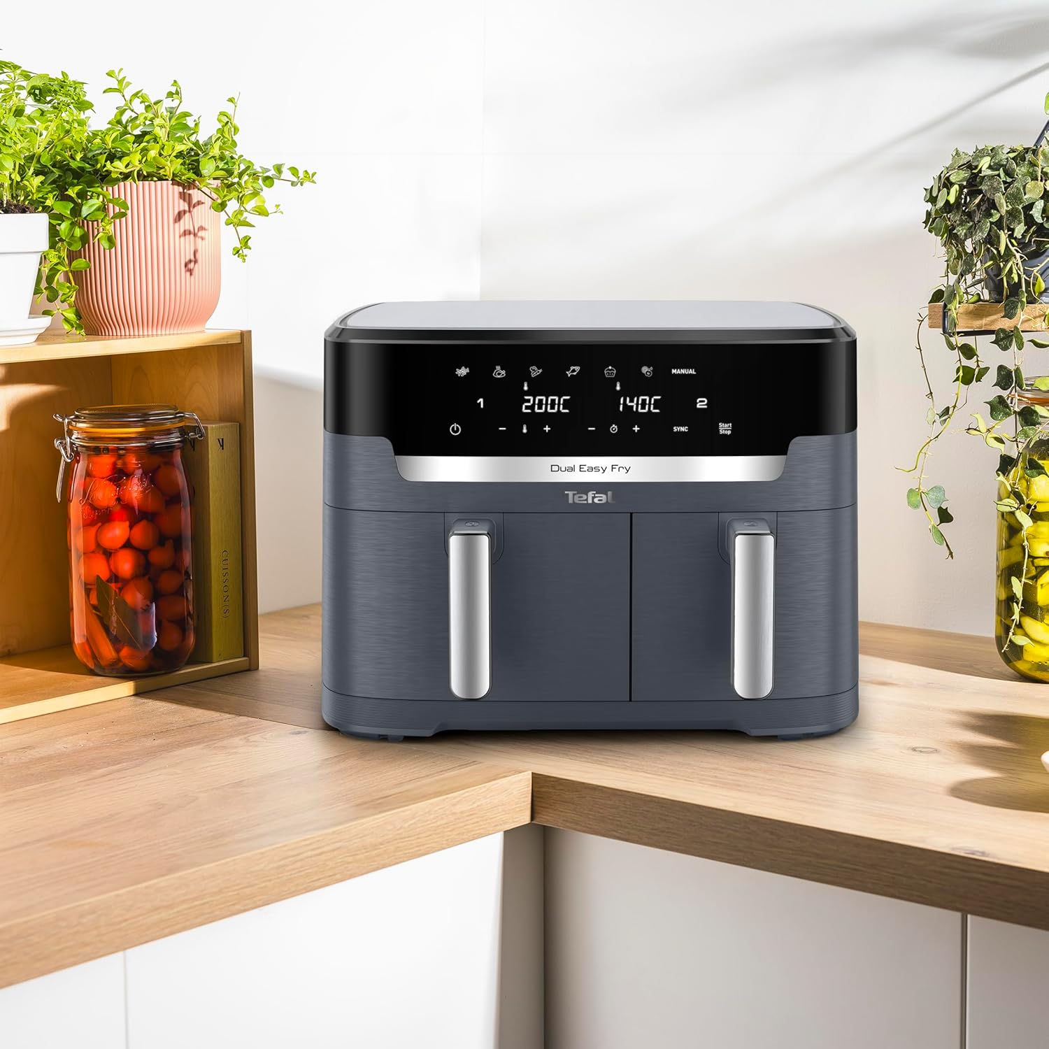 Le Tefal Dual Easy Fry XXL gris posé dans un angle de plan de travail en bois, entouré de plantes, montrant la place qu'il occupe en cuisine