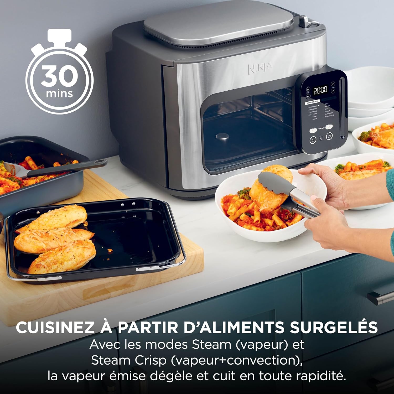 Ninja Combi SFP700EU posé sur un plan de travail, un repas complet de poulet et de pâtes servi dans des bols à côté du plateau de cuisson